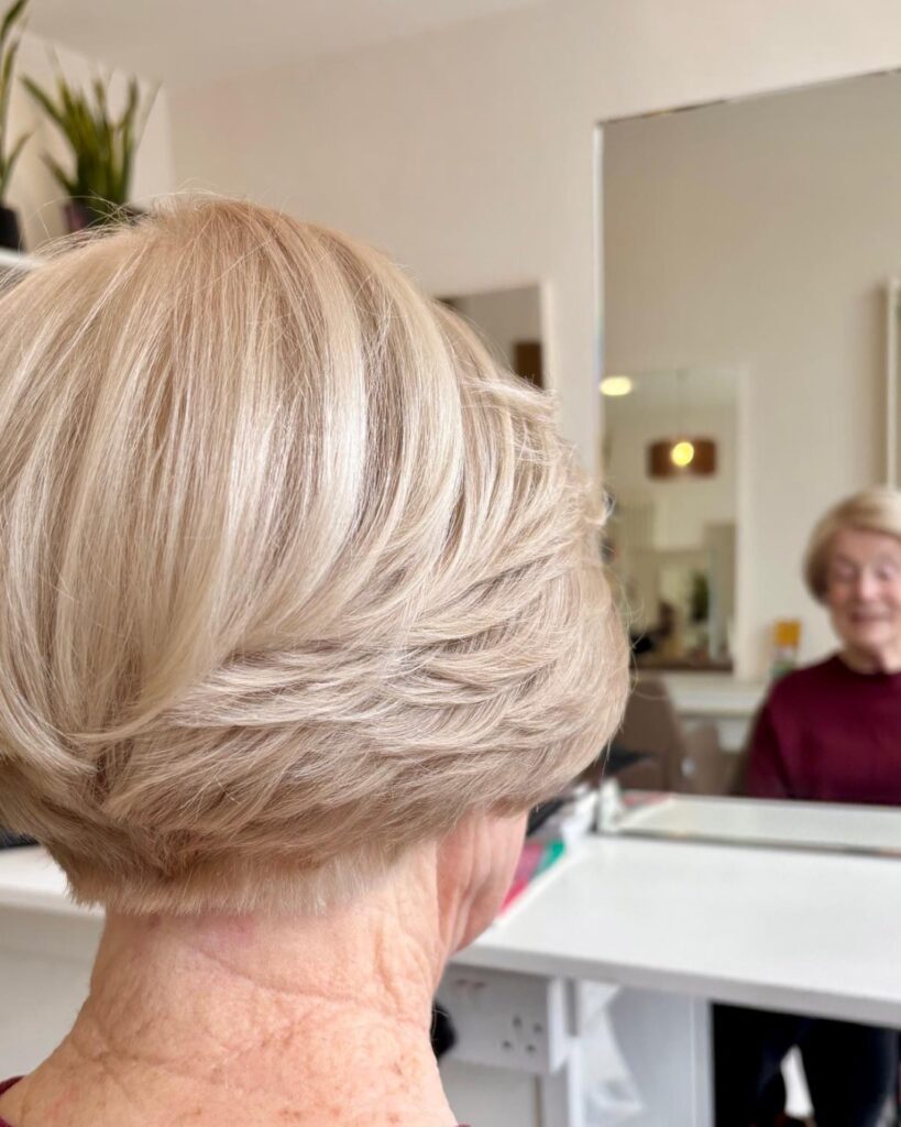 A back view of an older woman showcasing a feathered champagne blonde wedge haircut with stacked layers.