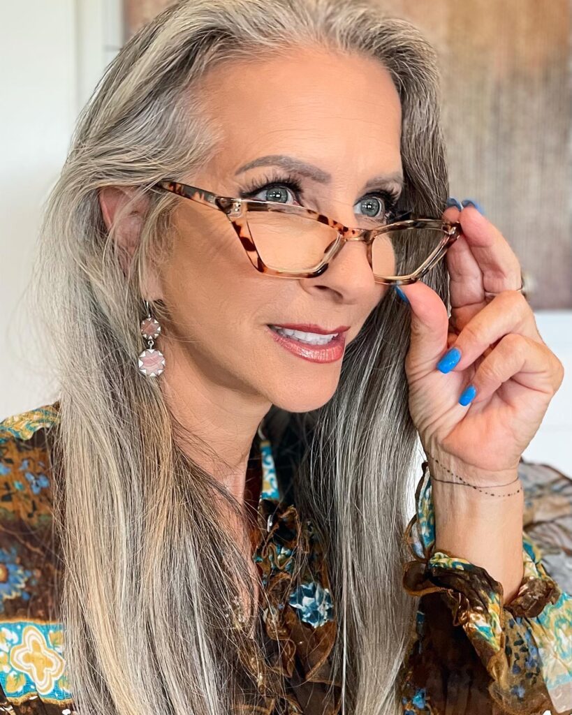 A close-up shot of a woman with long and straight silver-grey hair looking through tortoise-shell glasses.