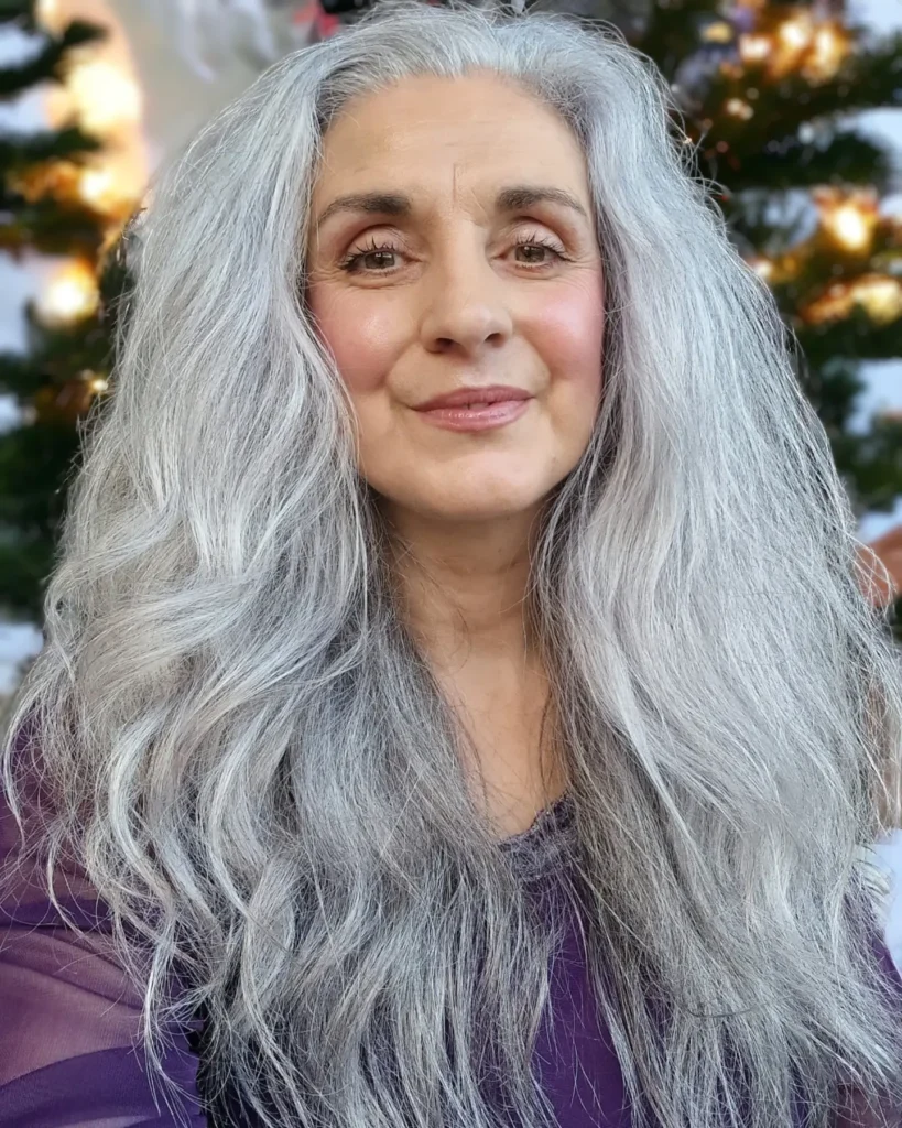 A smiling woman with voluminous long silver hair styled with a center part and soft waves framing her face.