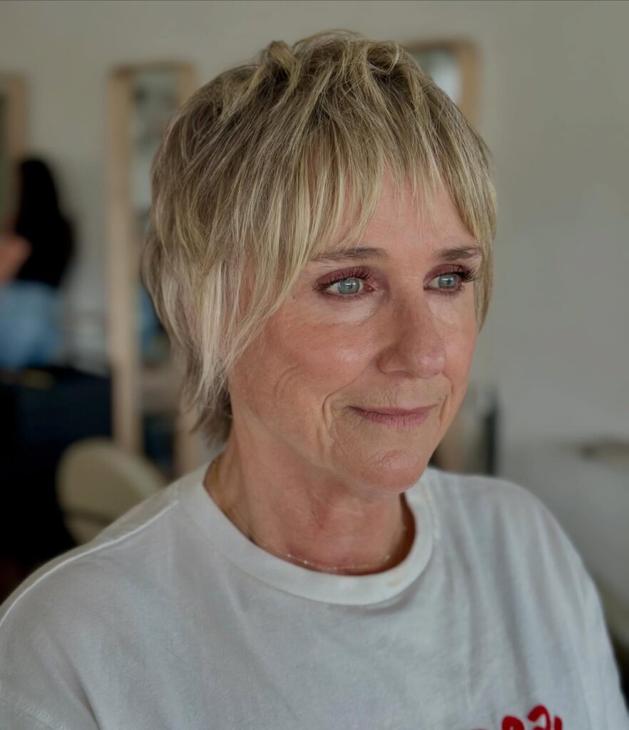 A woman over 60 looking to the side showcasing a textured blonde bixie hairstyle with a piecey fringe.