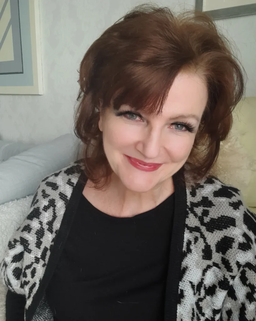 A smiling woman over 60 with a voluminous chestnut brown shag hairstyle featuring a side-swept fringe and textured layers.