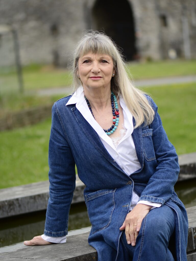 A woman with a neck length layered silver and blonde bob with side fringe wearing a white linen shirt and glasses outdoors.