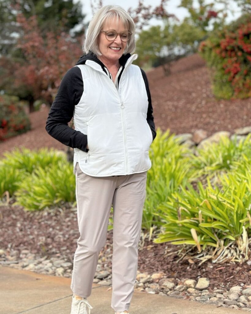 A woman with a short textured platinum pixie haircut styled to the side wearing a white top and a tan trench coat.