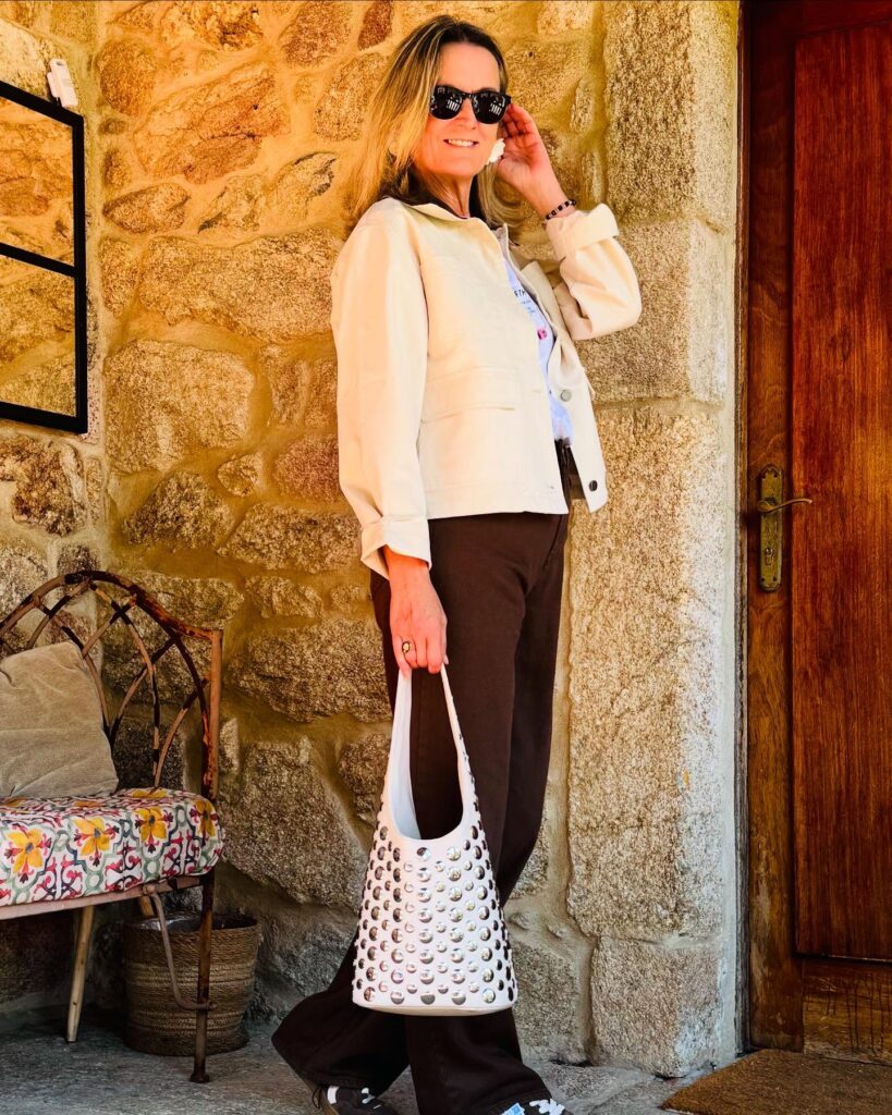 A woman with a shoulder-length layered blonde haircut and bright highlights wearing sunglasses and a cream jacket.