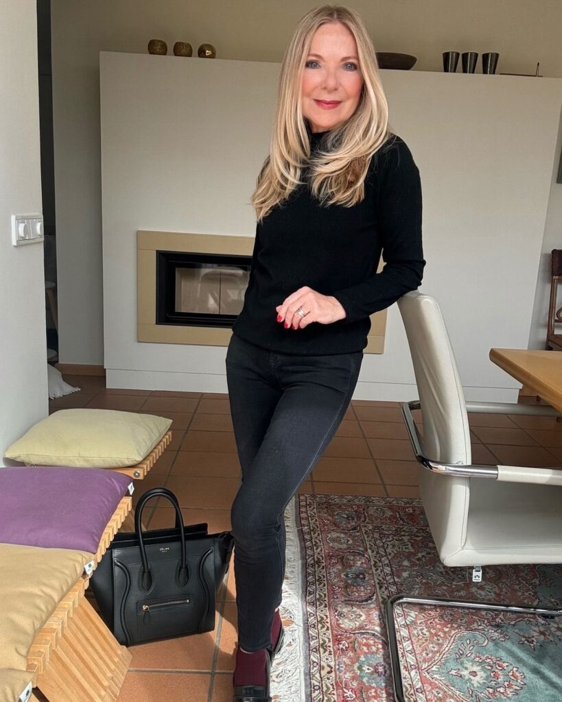 A woman with long straight blonde hair and long layers posing in a black long sleeve shirt.