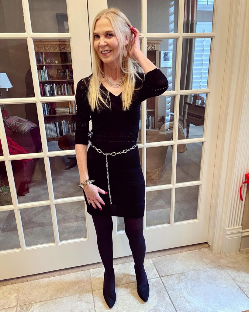 A woman over sixty with long straight pale blonde hair and a center part, tucking a strand behind her ear.