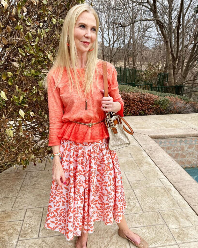 A woman with long straight icy blonde hair and a middle part posing outdoors.