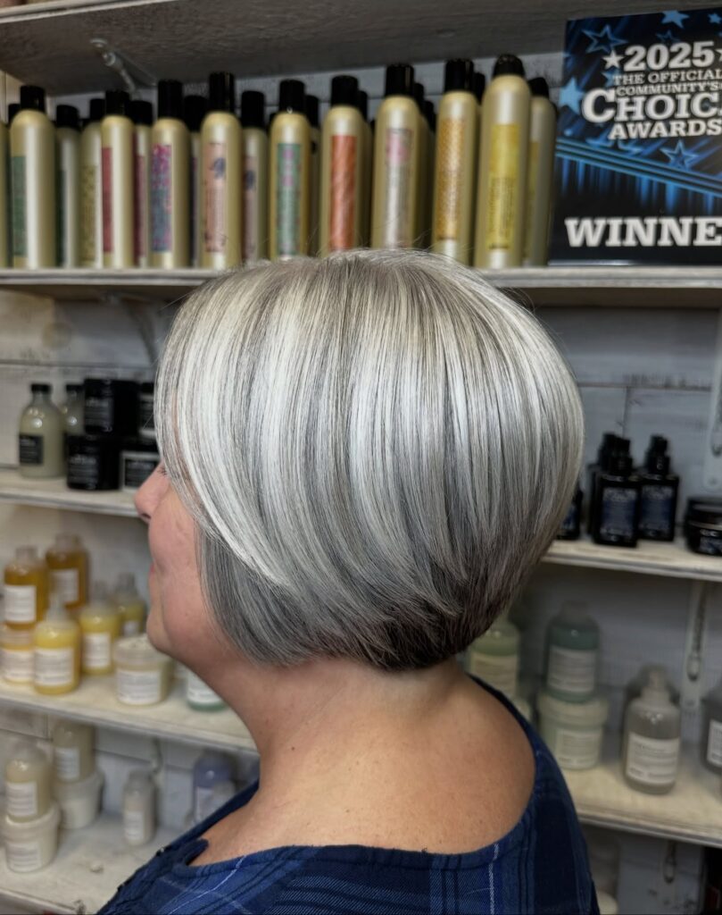 A side profile view of a woman showcasing a rounded, short-cropped haircut with blended silver and dark grey layers.
