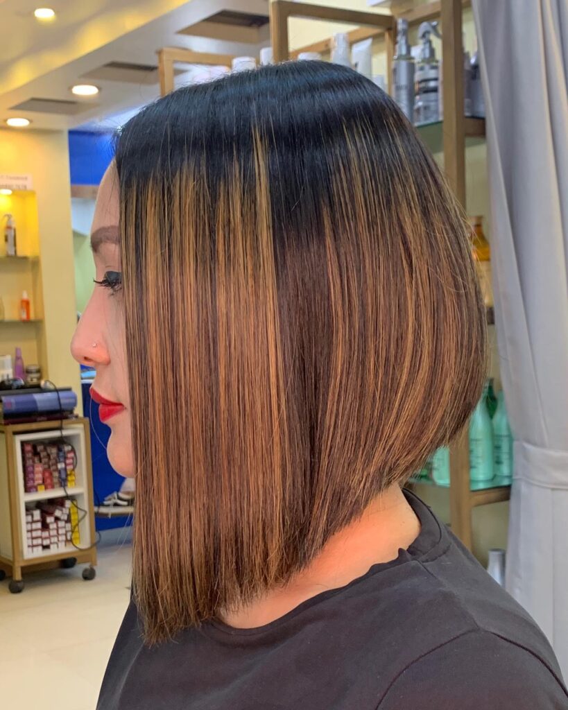 Straight angled bob with dark roots and warm caramel brown highlights.