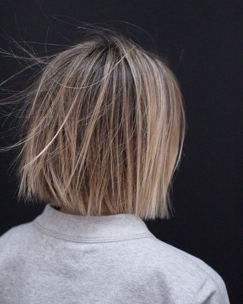 Textured blonde bob with dark roots and choppy straight layers.