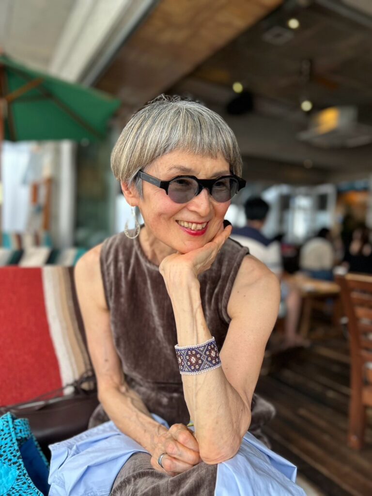 An older woman with a precision bowl cut in a salt-and-pepper grey color, featuring very short blunt bangs.