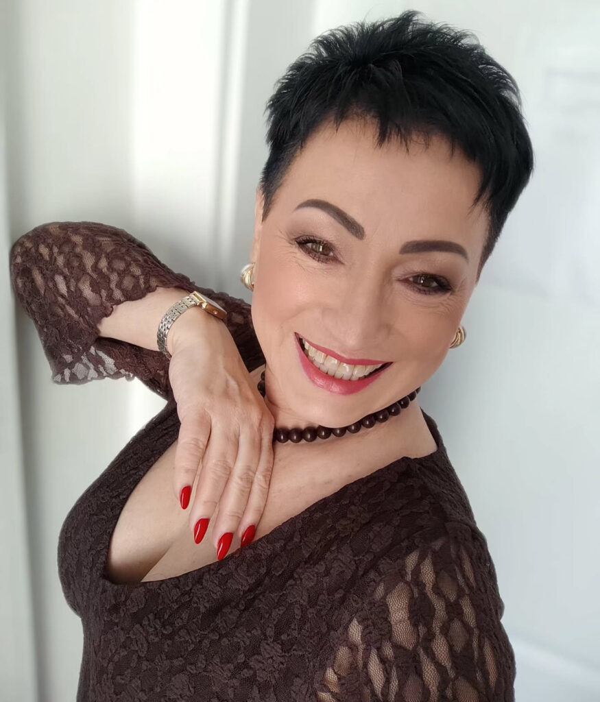 A smiling woman over 60 with a very short textured black pixie cut styled upwards and no bangs.