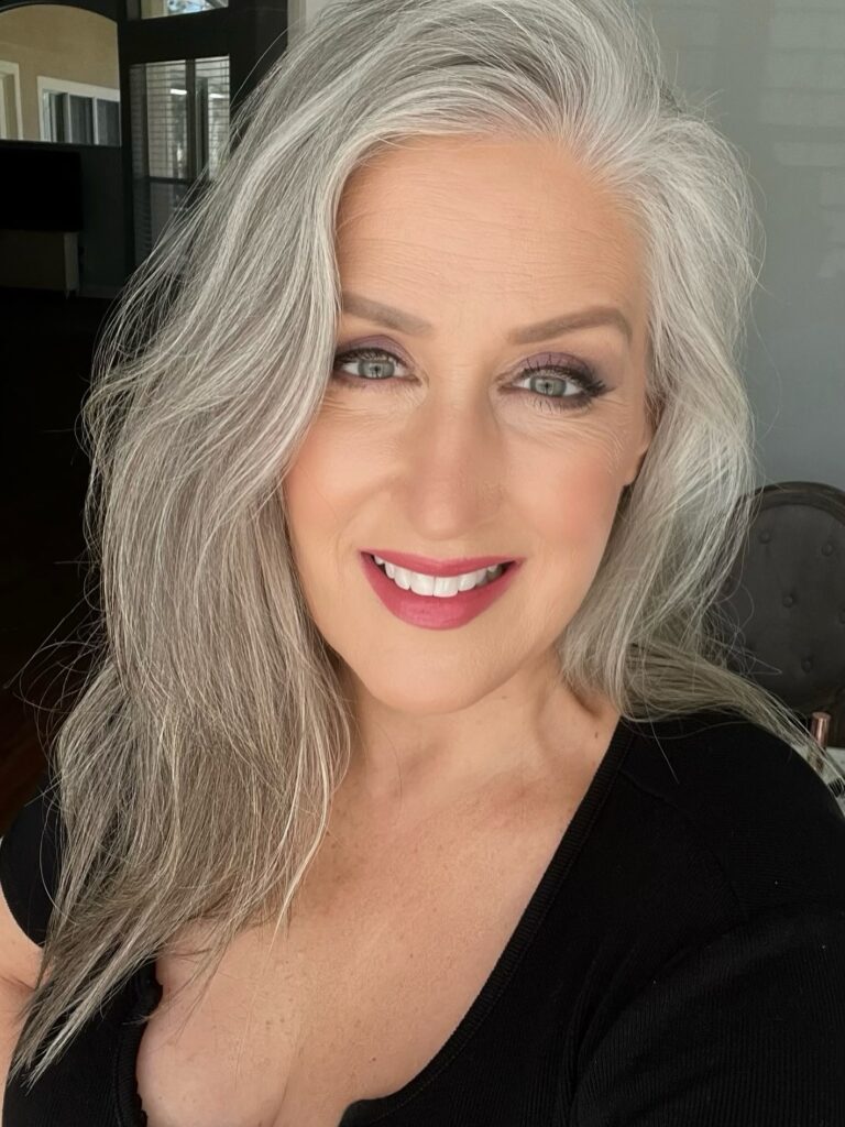 A woman with long, flowing, layered silver hair styled with a deep side part and no bangs.