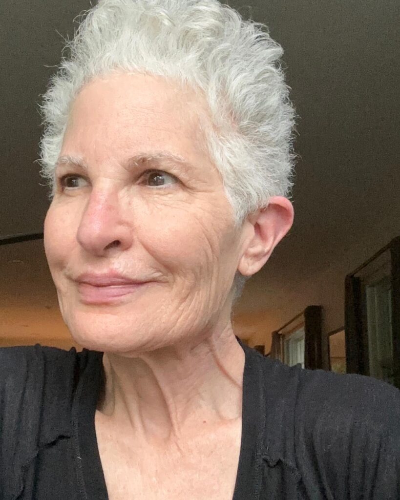 A woman with a short, spiky silver pixie cut featuring natural curls and no bangs.