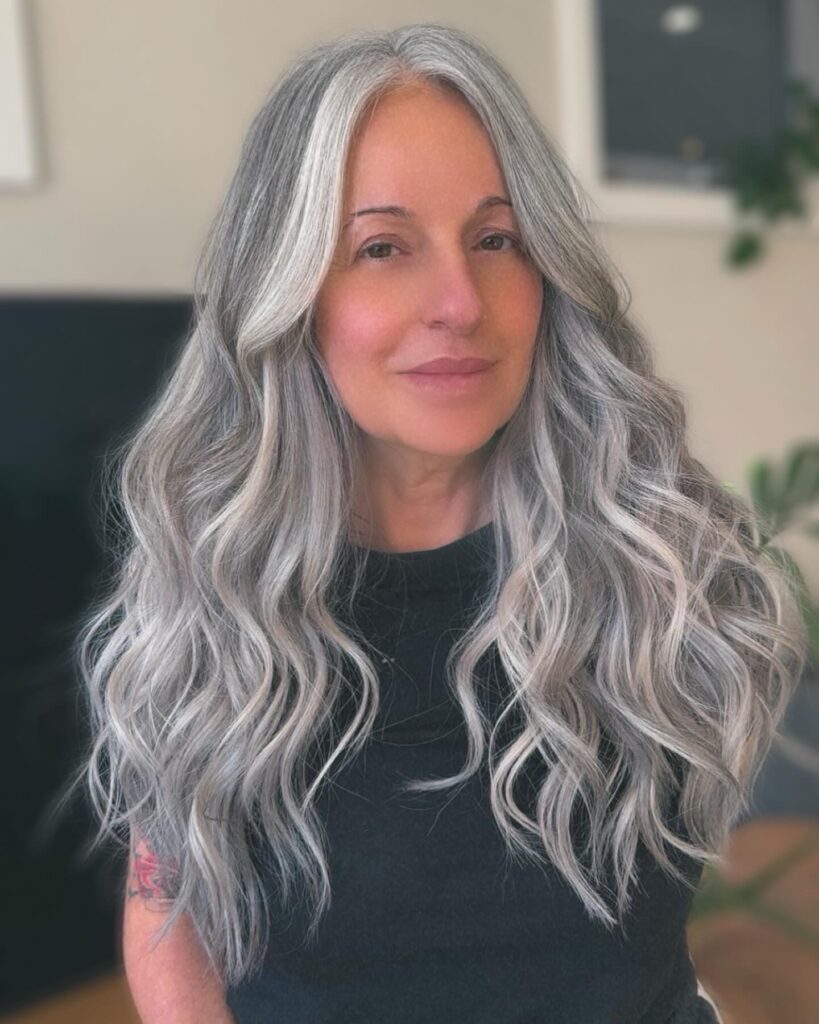 A woman with long, wavy, silver hair featuring bright white highlights framing her face.