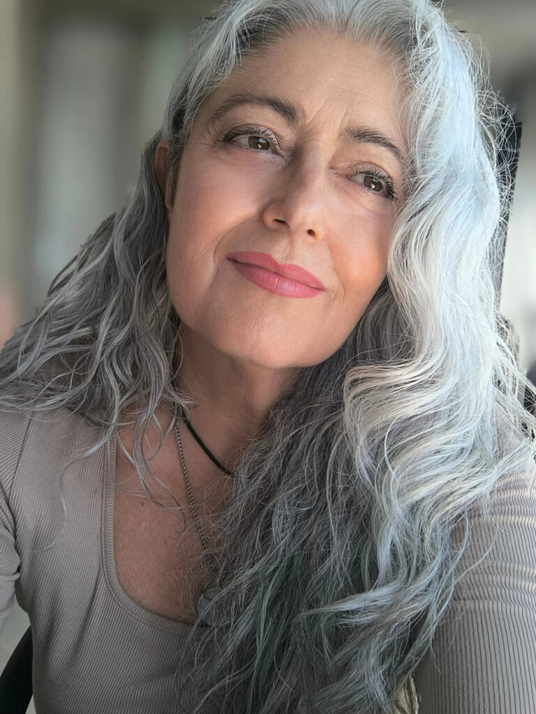 A woman with long, wavy salt-and-pepper hair featuring a mix of charcoal and silver tones.