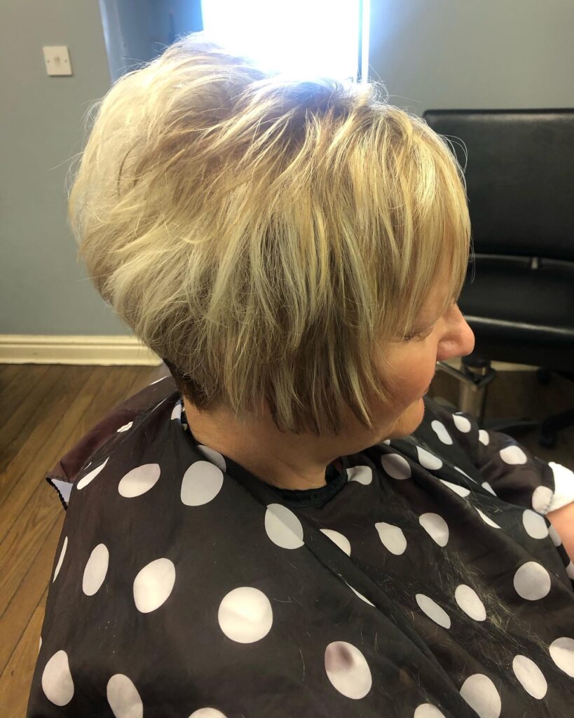 A woman over 60 with a short-stacked choppy bob in a bright blonde color with piecey layers and a tapered back.
