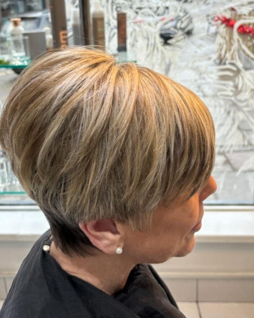 A woman over 60 with a short, tapered, choppy bob featuring golden highlights and voluminous layers.