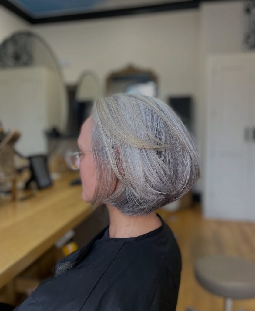 A woman with a sophisticated stacked, choppy bob in shades of silver and gray featuring a rounded back and jaw-length front.