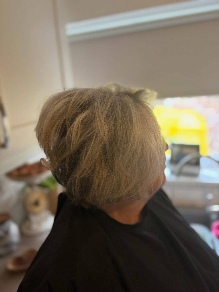 A woman with a short textured ash-blonde pixie bob featuring wispy layers and a voluminous crown.