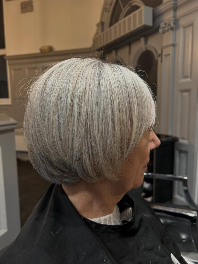 A woman over 60 with a rounded icy white choppy bob featuring a side-swept fringe and soft layered ends.