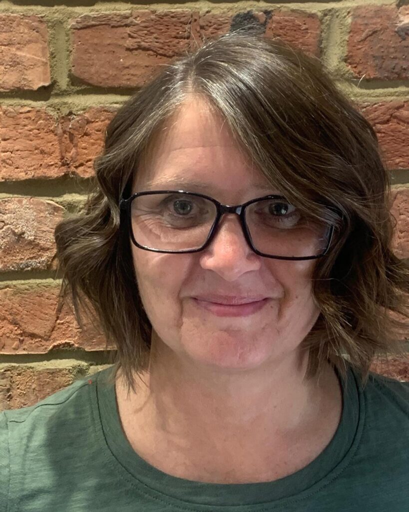 A woman over 60 with a wavy brunette bob featuring natural silver highlights and a side part.