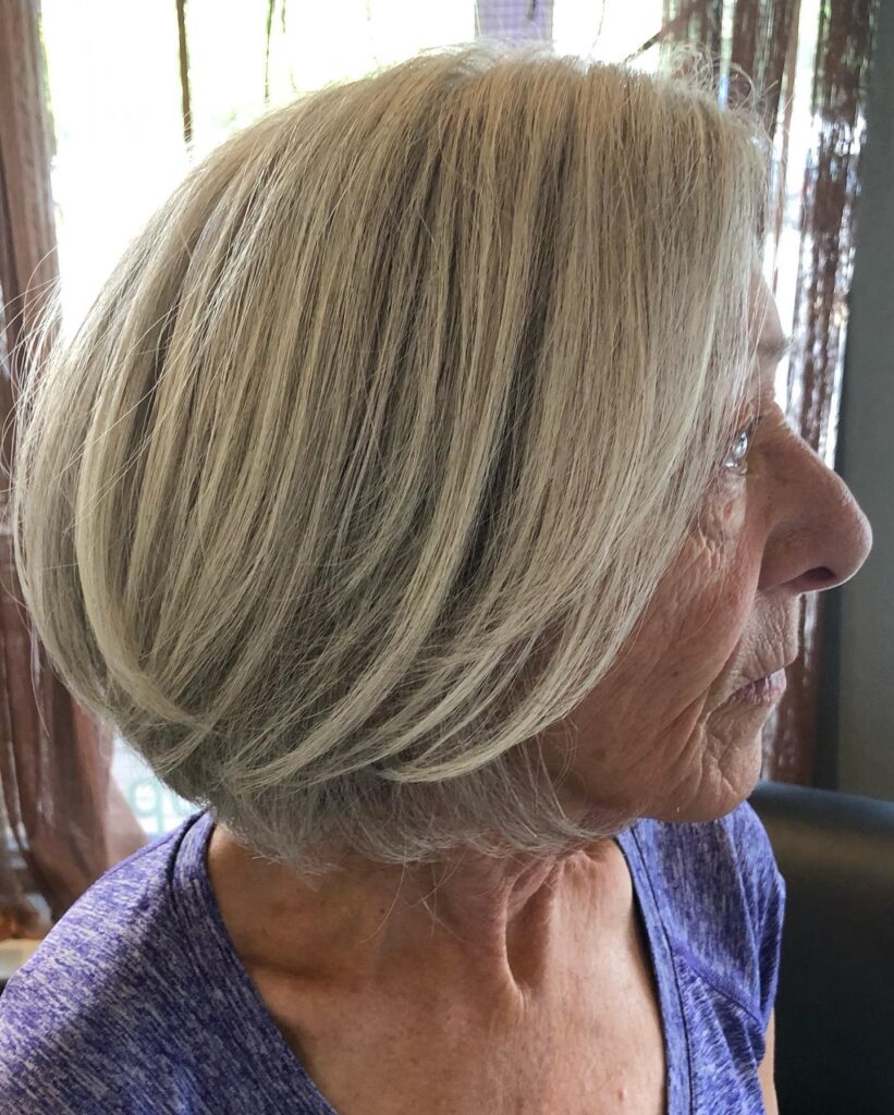 A woman over 60 is seen from the side with a sleek, rounded ash blonde bob that curves toward her chin.
