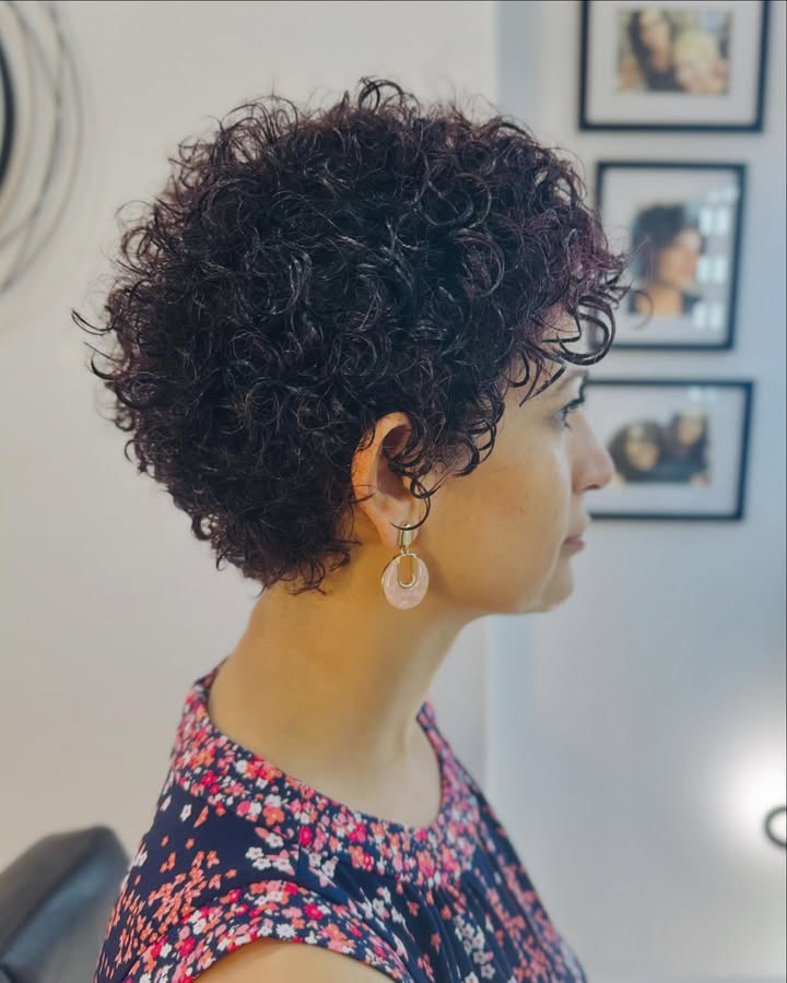 Short tapered curly pixie with defined curls on top and shorter sides.