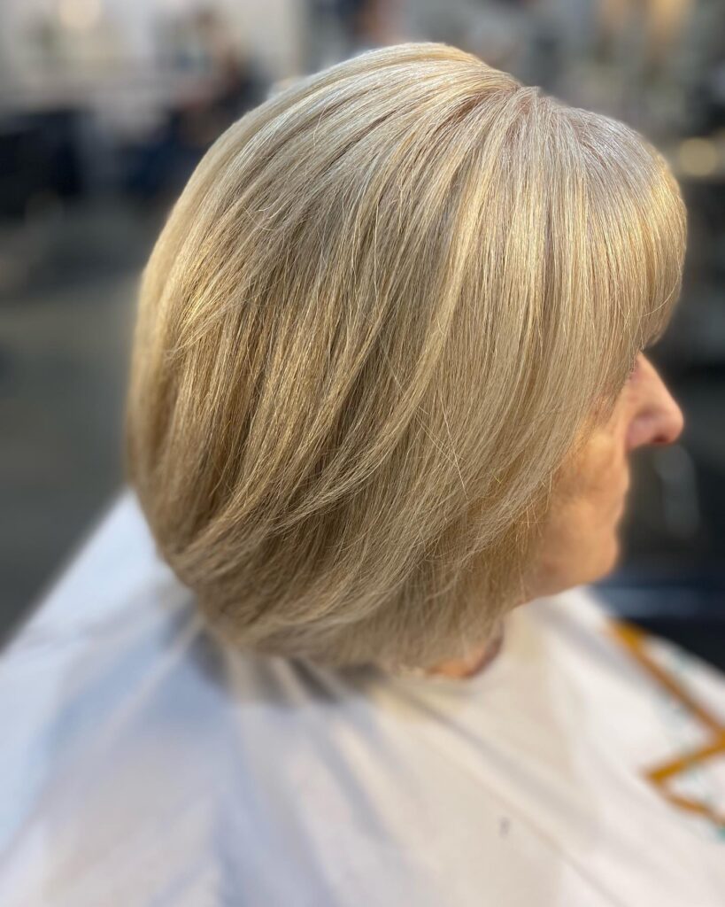 A woman over 60 with a short, sandy blonde, rounded bob featuring subtle layers and a smooth, polished finish.