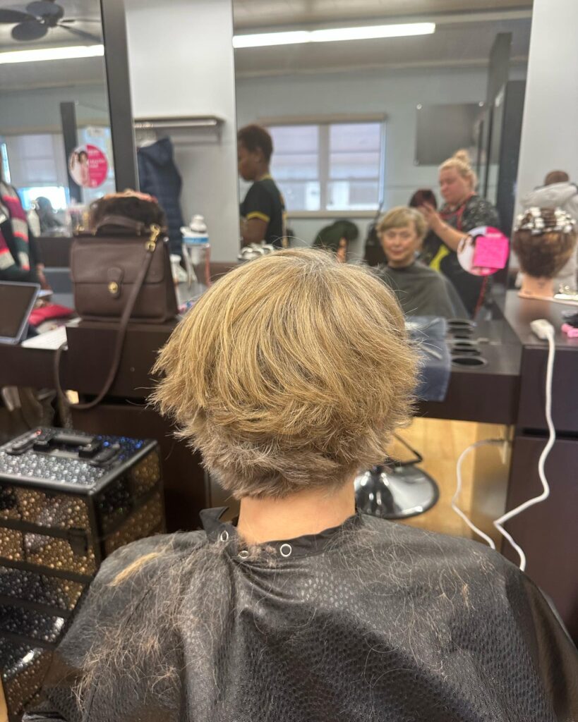 A back view of a woman with a short, messy pixie cut featuring choppy top layers and a tapered neckline.