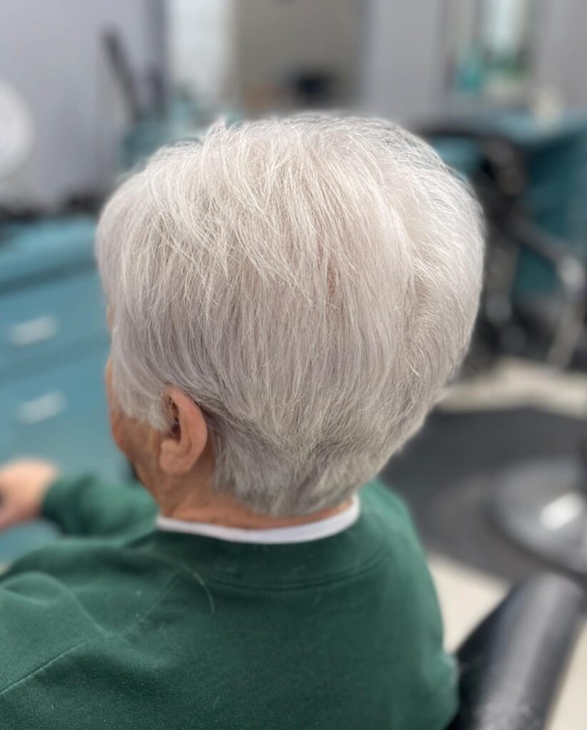 A side and back view of a woman with a classic silver pixie cut featuring soft, wispy layers and a neatly tapered neckline.