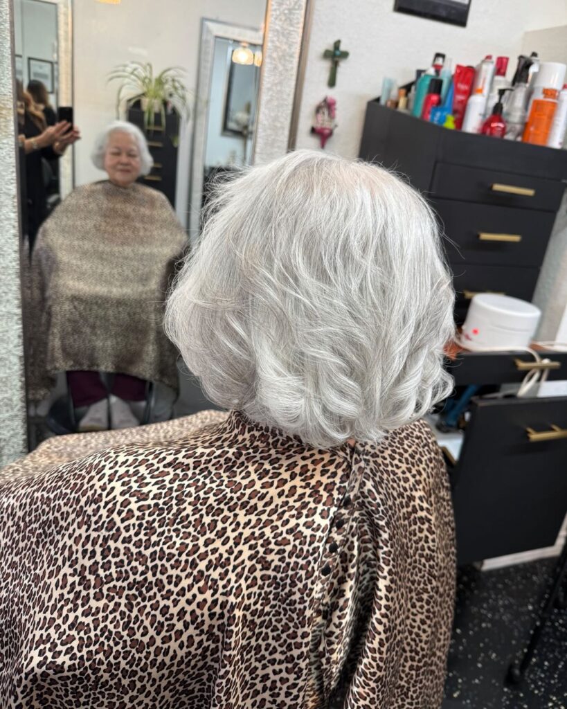 A rear view of a woman with a soft, feathered white bob featuring voluminous layers and curved ends.