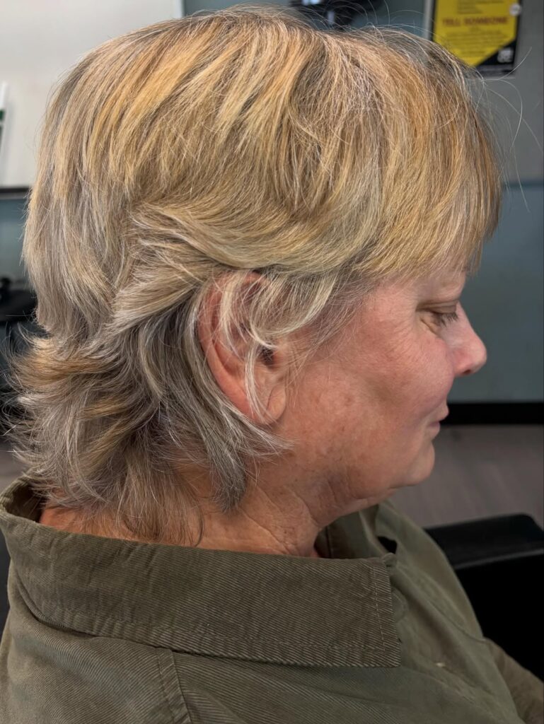 A side profile of a woman with a short, layered, shaggy haircut featuring flicked-out ends and golden blonde highlights.