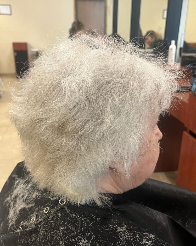 A side profile of a woman with a short, airy silver haircut featuring soft layers and a natural wavy texture.