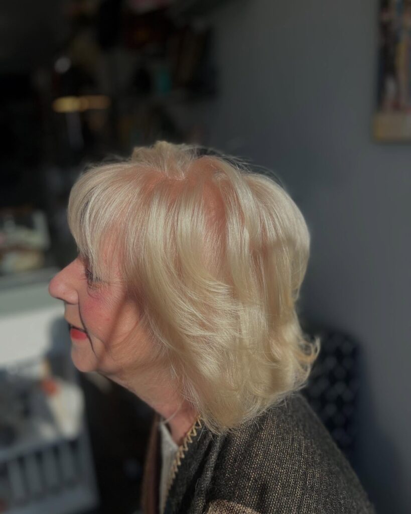 A woman over 60 with a shoulder-length layered lob in a creamy champagne-blonde color with soft waves.