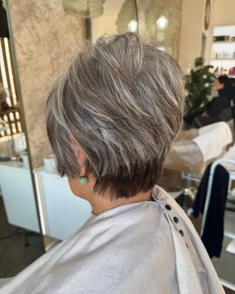 A woman with a short-stacked pixie cut featuring a blend of dark charcoal and bright silver layers.