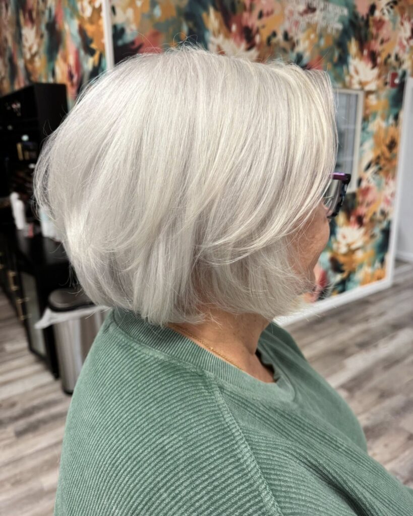A side profile of a woman over 60 with a bright platinum blonde layered bob and stylish glasses.