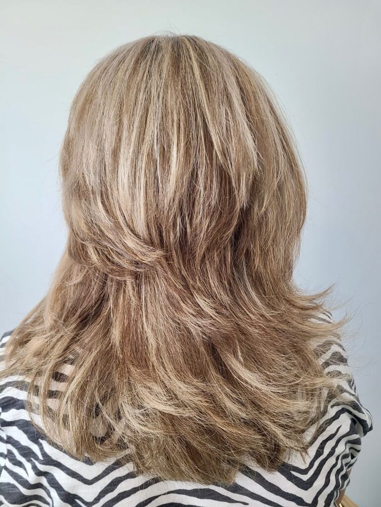 A rear view of a woman with shoulder-length sandy blonde hair featuring distinct tiered layers and flicked-out ends.