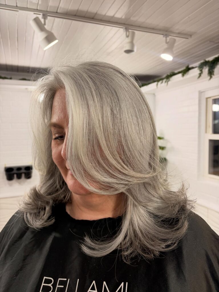 A woman over 60 with shoulder-length silver hair featuring long layers and ends curled inward for a rounded look.