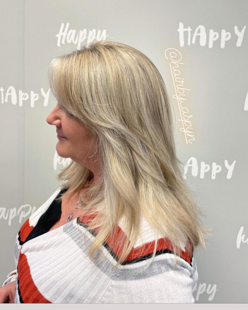 A side profile of a woman with medium-length blonde hair featuring soft tapered layers and bright highlights.