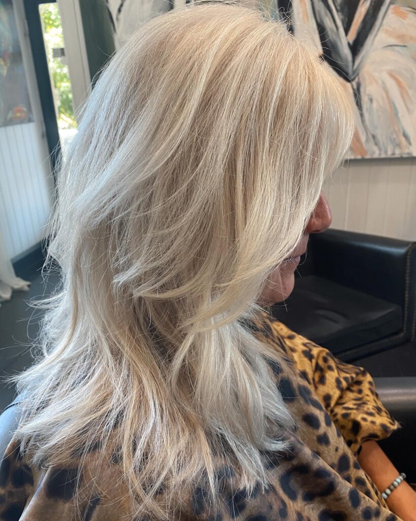 A side profile view of a woman with shoulder-length icy blonde hair featuring textured razor-cut layers and a feathered finish.