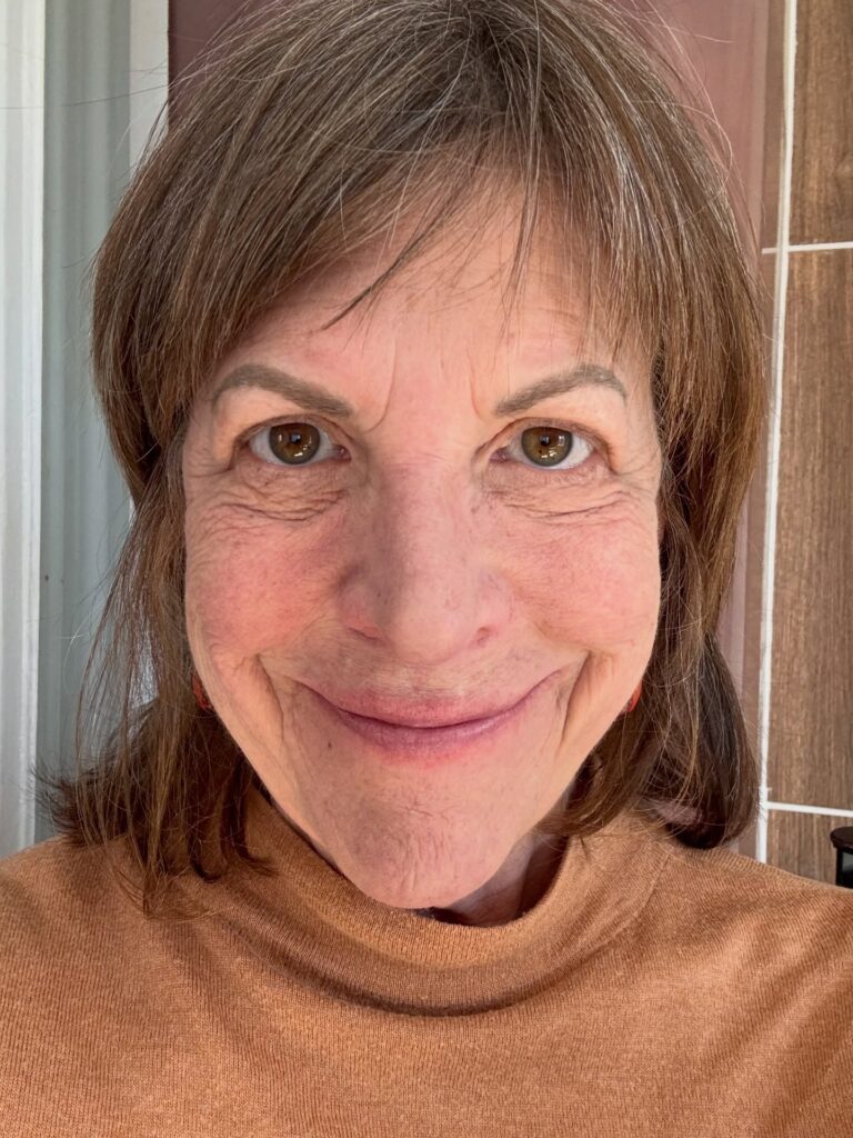 A woman with shoulder-length brunette hair and thin wispy bangs that rest just above her eyebrows.
