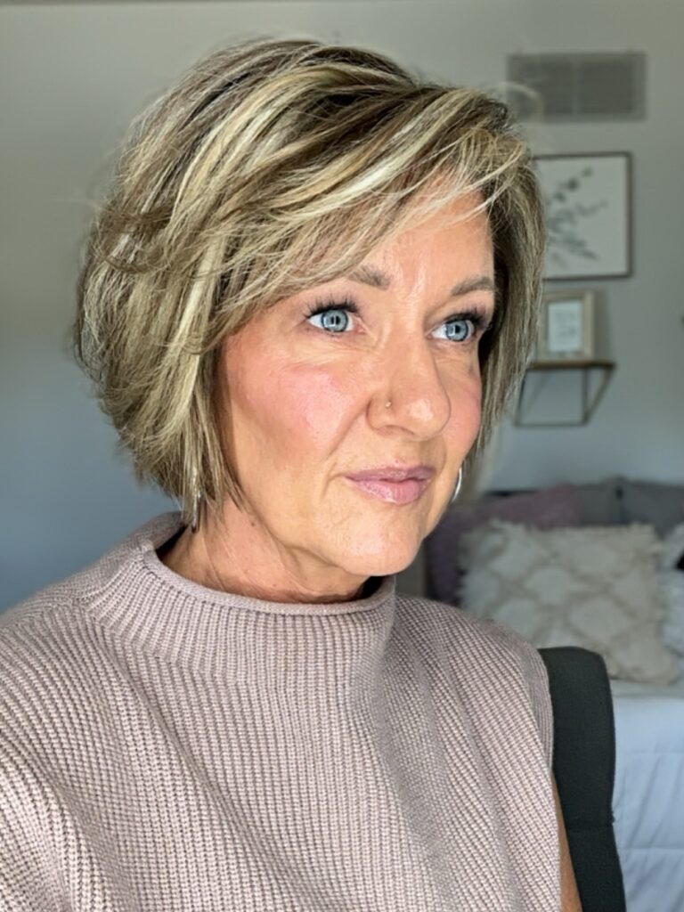 A woman with a dimensional bronde bob featuring blonde highlights and voluminous feathered side bangs.