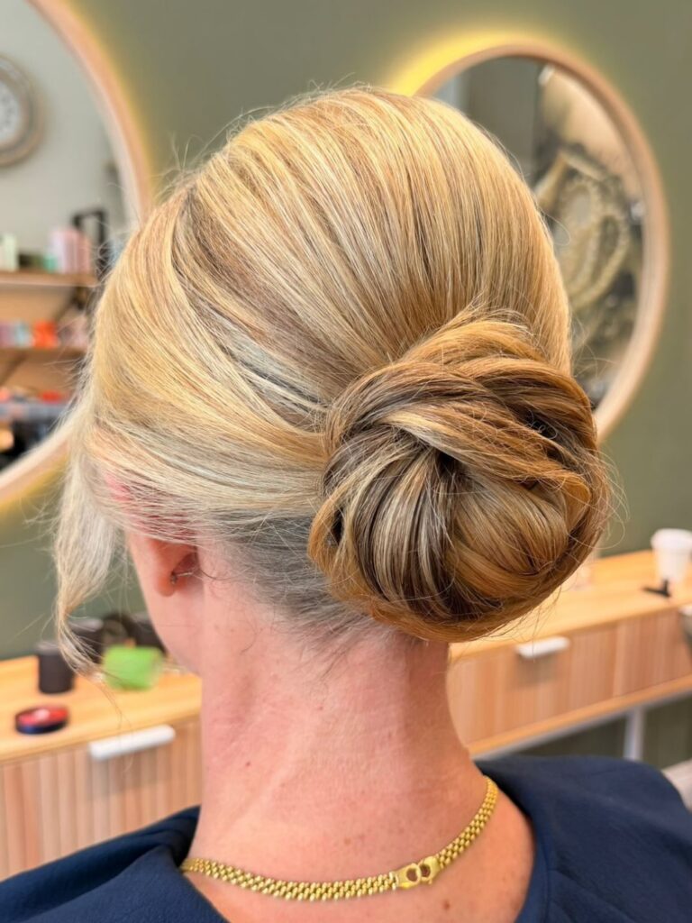 A woman with multitonal blonde hair gathered into a large textured low bun with soft pieces around the ears.