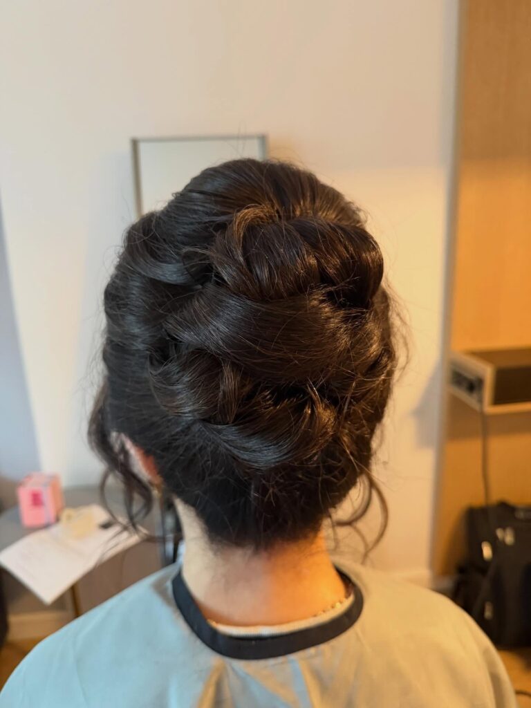A woman with dark hair has her locks styled in a low updo featuring soft loops and loose curled tendrils at the sides.