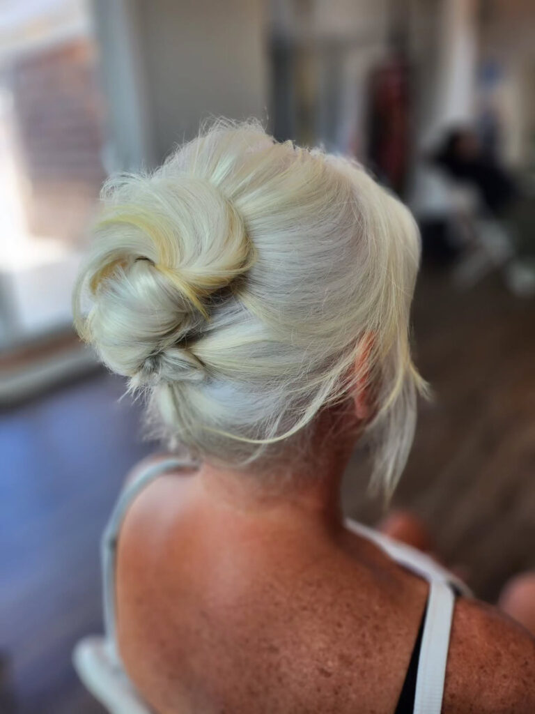 A woman with platinum blonde hair styled in a soft, airy twisted bun with loose, wispy pieces around the nape of her neck.