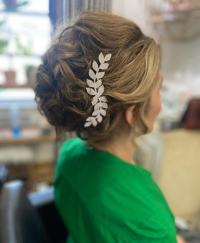 A woman with ash-blonde hair is seen from the side, wearing a soft twisted updo accented by a sparkling, silver leaf-shaped hair clip.