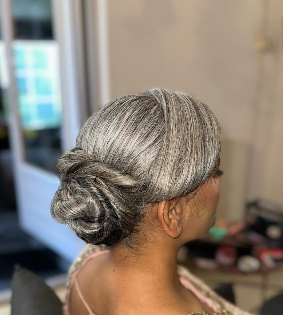 A woman with smooth silver and black hair is shown from a side profile, wearing a low updo styled into elegant circular swirls.