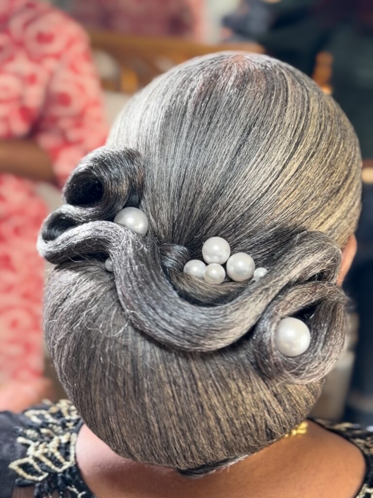 A woman with salt-and-pepper hair styled in sleek, sculptural waves adorned with several large white pearls.