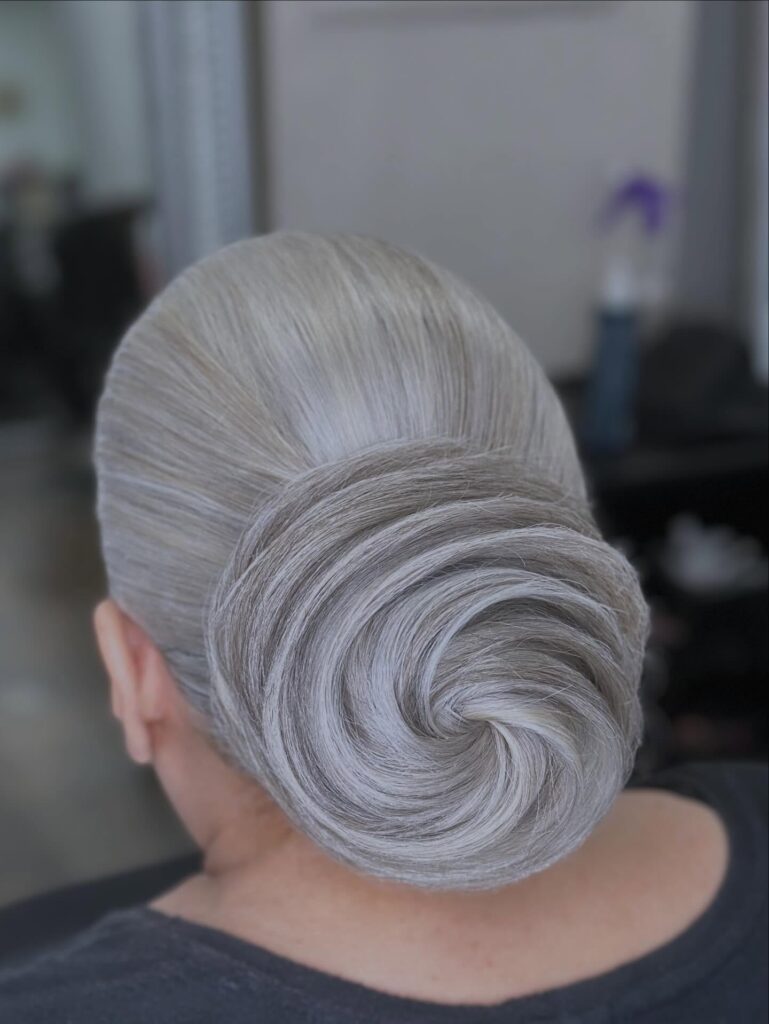 A woman with sleek silver hair styled in a large, intricate spiral chignon at the base of her head.